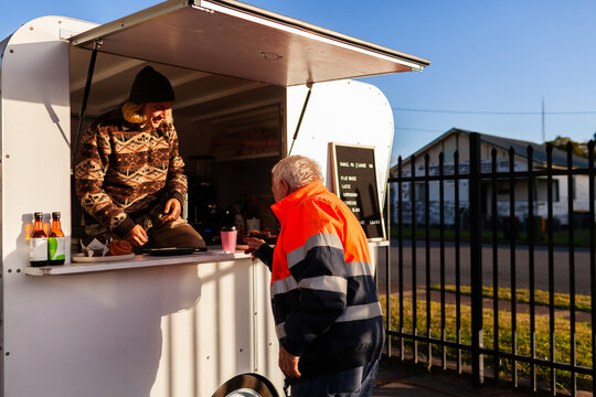Young barrister serving older customer from coffee van on sunlit winter morning