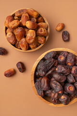 Delicious dried dates of different varieties in wooden bowls on brown background top view. Oriental fruit, date palm fruit, natural sweet dessert. Organic healthy snack, food background