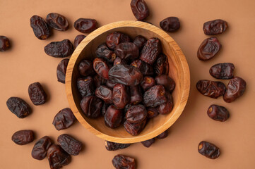 Delicious dried dates in wooden bowl on brown background flat lay top view. Oriental fruit, date palm fruit, natural sweet dessert. Organic healthy snack, food background