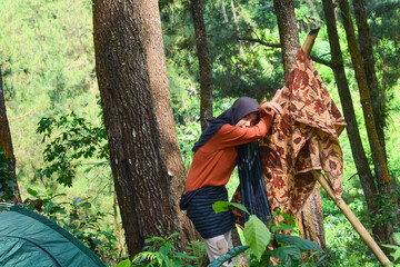 Young Asian Muslim woman hiking and camping in autumn forest, smiling at camera wearing Javanese...