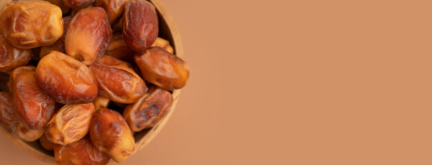 Delicious dried dates in wooden bowl on brown background flat lay top view. Oriental fruit, date palm fruit, natural sweet dessert. Organic healthy snack, food background