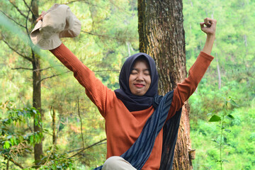 Young Asian Muslim woman hiking and camping in autumn forest, smiling at camera wearing Javanese...