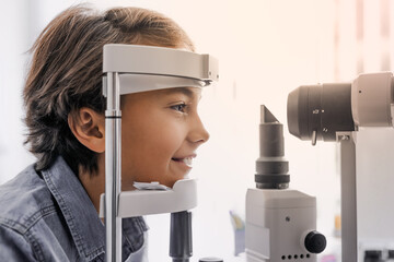 Side view shot of boy checking vision with tonometer at eye clinic. Glasses prescription, eyesight check vision examination in modern clinic with apparatus medical equipment