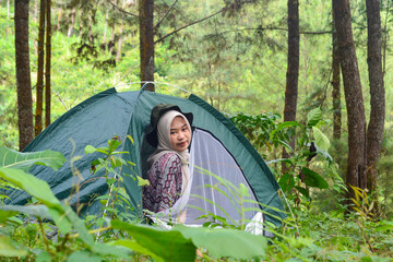 Sporty Muslim Asian woman standing near tent and backpack, enjoying sunny afternoon in the mountains. Camping lifestyle concept