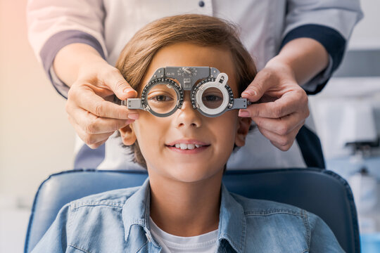 Smiling child boy in glasses checks eye vision at pediatric ophthalmologist. Small patient undergoing eye sight correction, choosing lenses frame for glasses in clinic hospital
