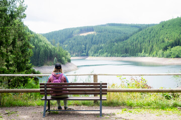 Traveler with backpack sitting on bench, enjoying peaceful mountain lake view and pine forest. Concept of relaxation, mindfulness, and adventure in nature.