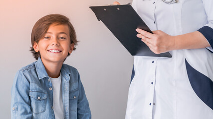 Cropped image of school boy and doctor have consultation in hospital room. Pediatrician medical worker nurse taking notes of diagnosis, medical treatment drugs medicine prescription in clipboard