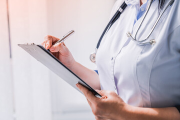 Female doctor with stethoscope writing prescription on clipboard. Cropped photo of nurse medical worker taking notes, noting diagnosis, test results, medical prescription, side effect of drugs history