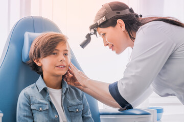 Fototapeta premium Professional otolaryngologist examining boy in medical clinic. Nose and mouth ear cavity health checkup treatment. Larynx, laryngitis, hearing problems
