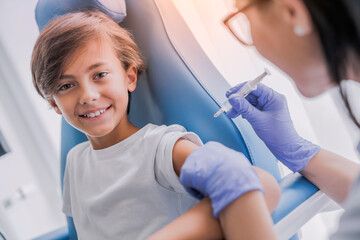 Vaccination concept. Female doctor vaccinating cute smiling little boy in clinic against measles,...