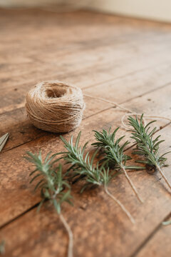 Rosemary plant cuttings and twine on timber surface