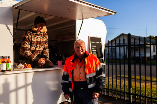happy older Aussie workman in high vis workwear buying warm takeaway coffee from van