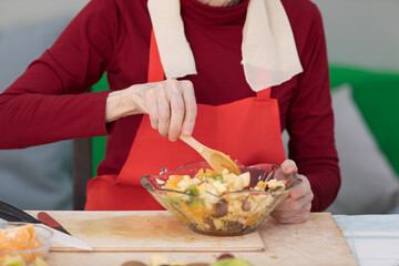 Elderly woman preparing fruit salad at home in the living room