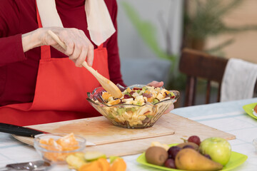 Elderly woman preparing fruit salad at home in the living room