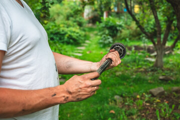 Car mechanic examining a used axle shaft with a constant-velocity joint, performing essential repairs outdoors in a summer garden
