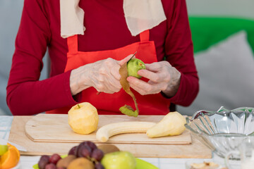 Elderly woman preparing fruit salad at home in the living room