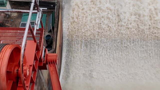 Dam floodgate releasing turbulent water with spray and mist, showing flood discharge power.