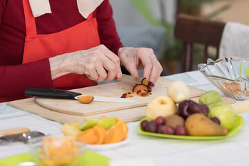 Elderly woman preparing fruit salad at home in the living room