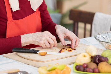Elderly woman preparing fruit salad at home in the living room