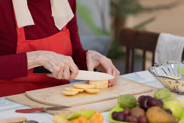 Elderly woman preparing fruit salad at home in the living room