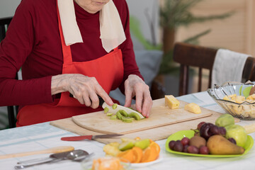 Elderly woman preparing fruit salad at home in the living room