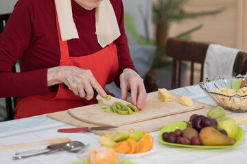 Elderly woman preparing fruit salad at home in the living room