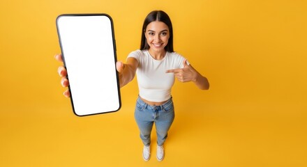 Smiling Woman Pointing to Smartphone on Yellow Background Mobile Technology Concept for Online Marketing & Promotion