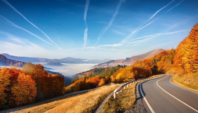 calm landscape with autumn road and orange forest under blue sky mountains landscape in fall season with morning fog and winding roadway