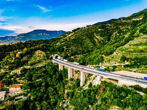 Aerial view of highway road with tunnel in mountains. Traffic on the road, cargo trucks logistic and hybrid electric cars driving viaduct road in Italy