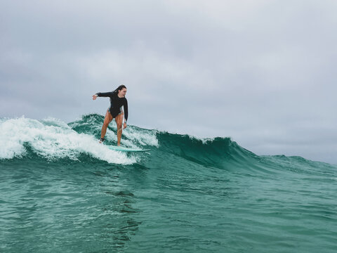 Woman surfing wave on overcast day in spring suit wetsuit on mid length board