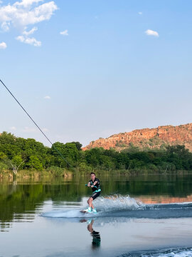 Boy wakeboarding on glassy Ord River with red rocky outcrop and lush foliage lining banks