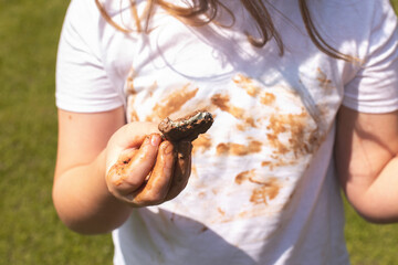 Girl child staining her white t-shirt with stain while enjoying a delicious chocolate bar in garden