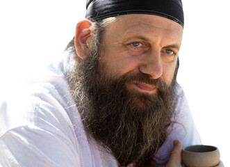 A bearded man in a bandana is drinking tea on the background of nature.