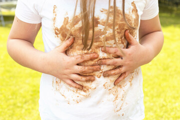Girl child staining her white t-shirt with stain while enjoying a delicious chocolate bar in garden