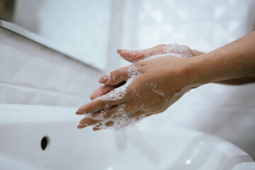 Fototapeta premium A woman washes hands with soap and water in a bathroom sink, creating bubbles and foam for hygiene, health, and cleanliness.