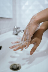 A woman washes hands with soap and water in a bathroom sink, creating bubbles and foam for hygiene, health, and cleanliness.