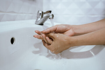 A woman washes hands with soap and water in a bathroom sink, creating bubbles and foam for hygiene,...