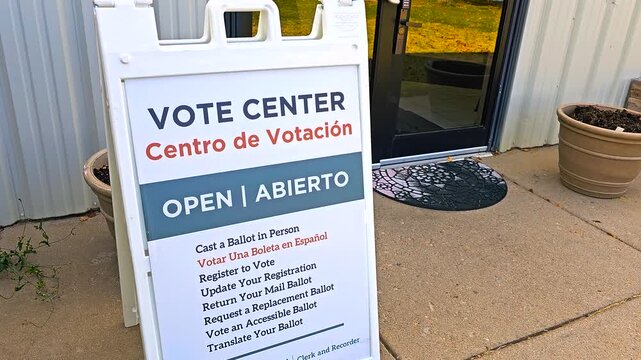 Stock video of a bilingual sign &ldquo;Vote Center &ndash; Open, Abierto, Centro de Votaci&oacute;n&rdquo; with Spanish translation, capturing election inclusivity, voter registration, in-person access, mail ballot drop-offs
