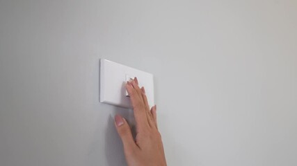 A person presses a light switch indoors, using their finger to control electricity, promoting energy saving, safety, and environmental conservation.