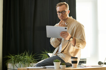 Handsome young businessman focuses on digital tablet while working in a modern office environment