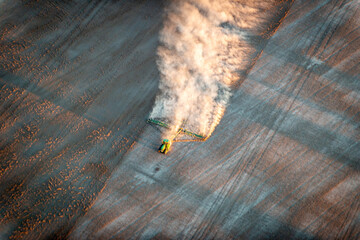blurred tractor trailing dust across a dry paddock in early morning light, viewed from above
