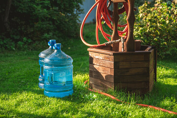Two large water bottles sit on a lush green lawn next to a decorative wooden well with a red garden...