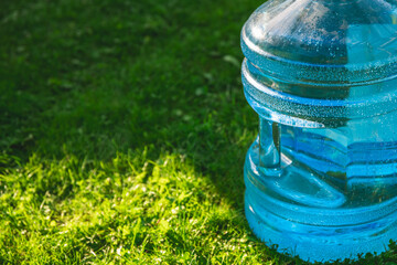 Fototapeta premium Big blue plastic bottle filled with clean drinking water, resting on vibrant green grass under the warm summer sunlight, offering refreshing hydration and promoting wellness in nature