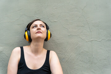 Blonde woman 40s in yellow headphones lost in music, close-up urban portrait