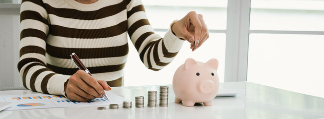 A woman analyzes financial charts while saving money, with stacked coins and a piggy bank...