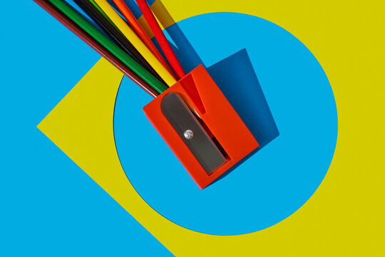 Big red pencil sharpener with colored pencils on yellow and blue background