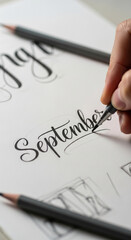 Close-up of hand lettering "September" in progress, showcasing elegant calligraphy style with pencil and paper, representing creativity, artistry, and hand-drawn design