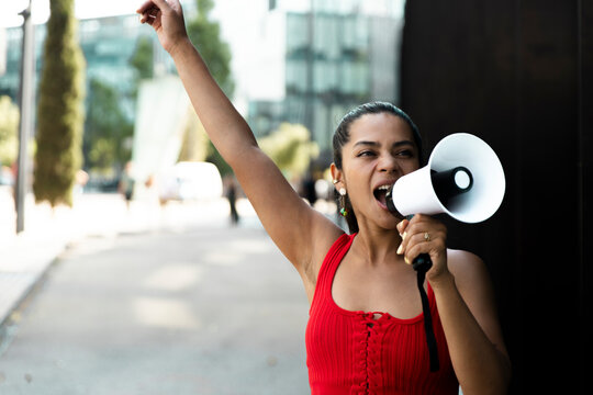 Activist in red outfit shouting with megaphone in urban street protest
