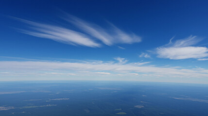 An aerial view of a beautiful blue sky with wispy white clouds over the ocean. This serene and expansive scene represents freedom, tranquility, and travel.
