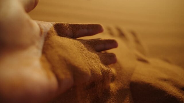 Close-up of golden desert sand flowing gently through fingers at sunset in the Sahara Desert, Morocco, with warm light highlighting the fine grains.